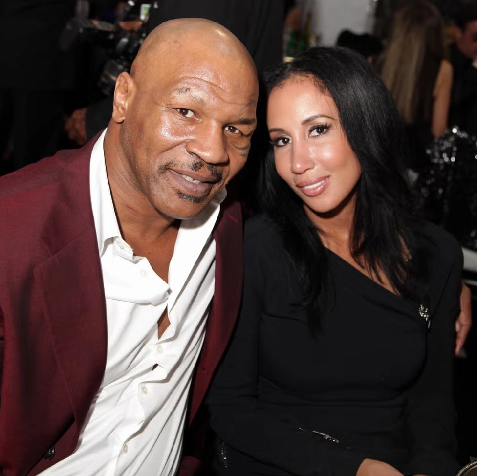 Mike Tyson mặc áo vest đỏ và Kiki Spicer mặc đồ đen mỉm cười trước ống kính khi ngồi cạnh nhau